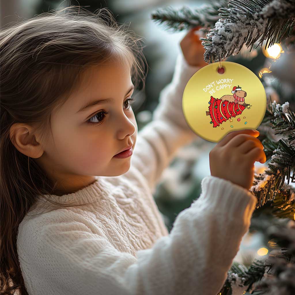 Gold round capybara ornament on a tree, showing 'DON'T WORRY BE CAPPY' and red artwork