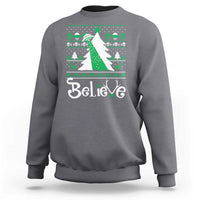 Gray crewneck sweatshirt with festive 'Believe' print and green bow UFO graphic