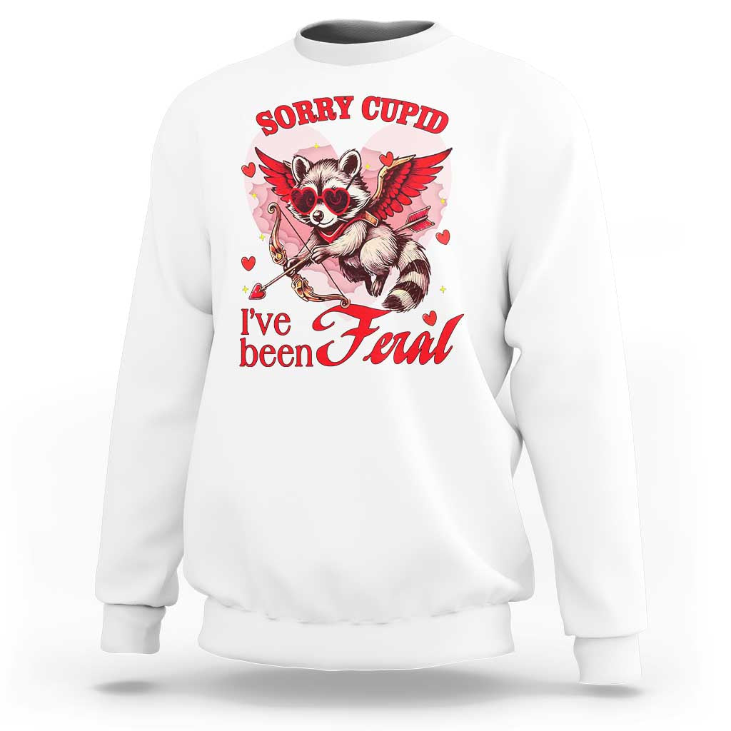 White unisex sweatshirt with Cupid raccoon graphic and red “I've been feral” text
