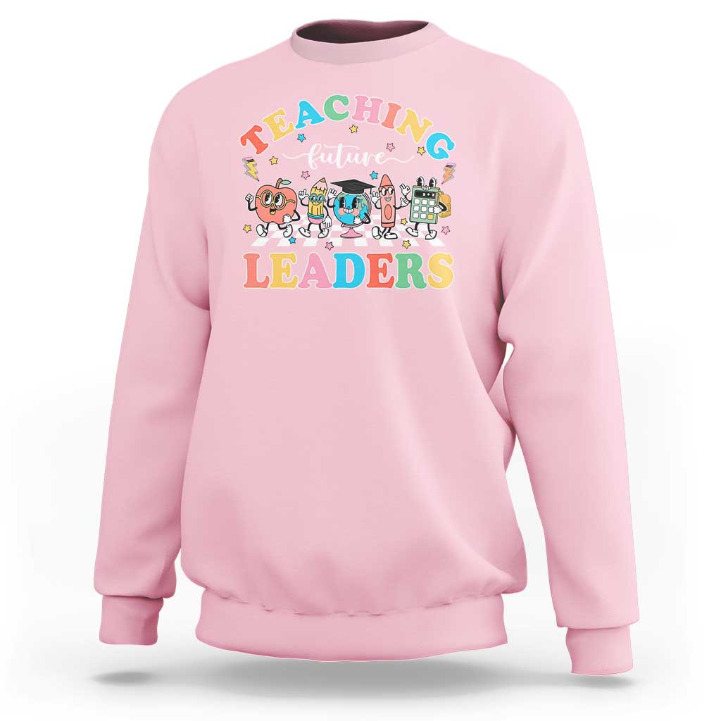 Light pink teacher sweatshirt with colorful “Teaching Future Leaders” character graphic
