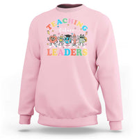 Light pink teacher sweatshirt with colorful “Teaching Future Leaders” character graphic