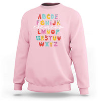 Light pink sweatshirt with cute monster alphabet A–Z graphic on front.