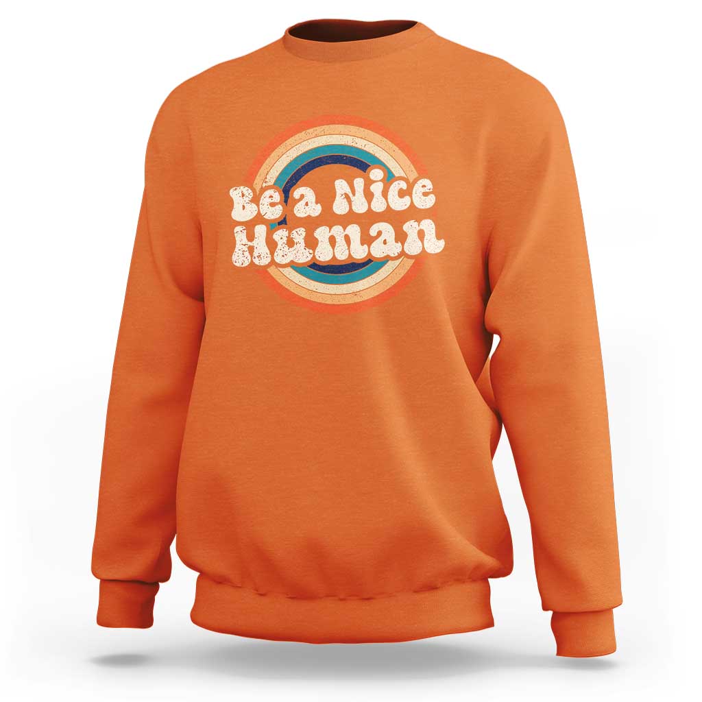 Orange crewneck sweatshirt with 'Be a Nice Human' rainbow graphic