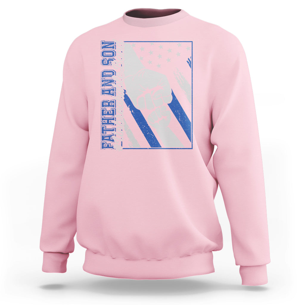Light pink crewneck sweatshirt with blue chest graphic of two fists and stars.