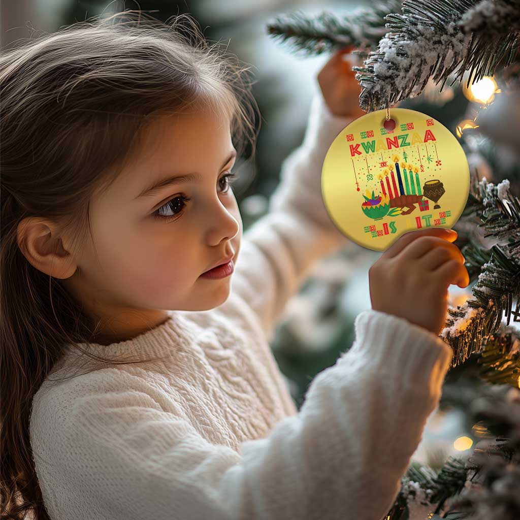Gold round Kwanzaa ornament held near a Christmas tree, with candles and “Kwanzaa”