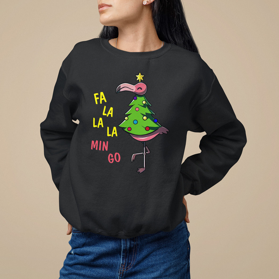 Black sweatshirt with flamingo beside decorated Christmas tree and “FA LA LA MIN GO” lettering