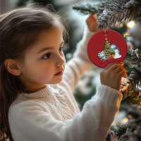 Red round axolotl Christmas ornament with tree scene, held by a child near pine