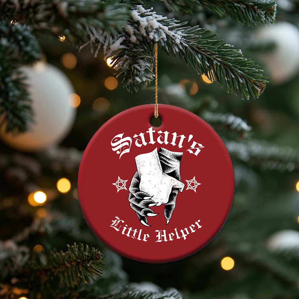 Red round Satan's Little Helper ornament hanging from a Christmas tree branch