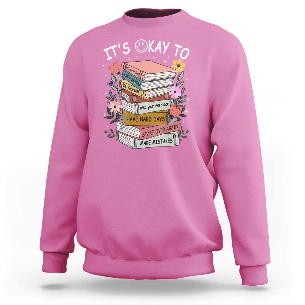 Pink sweatshirt with crew neck and “It’s Okay To” book graphic on the front