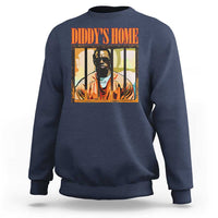 Navy crewneck sweatshirt with “DIDDY’S HOME” graphic and portrait print on chest.