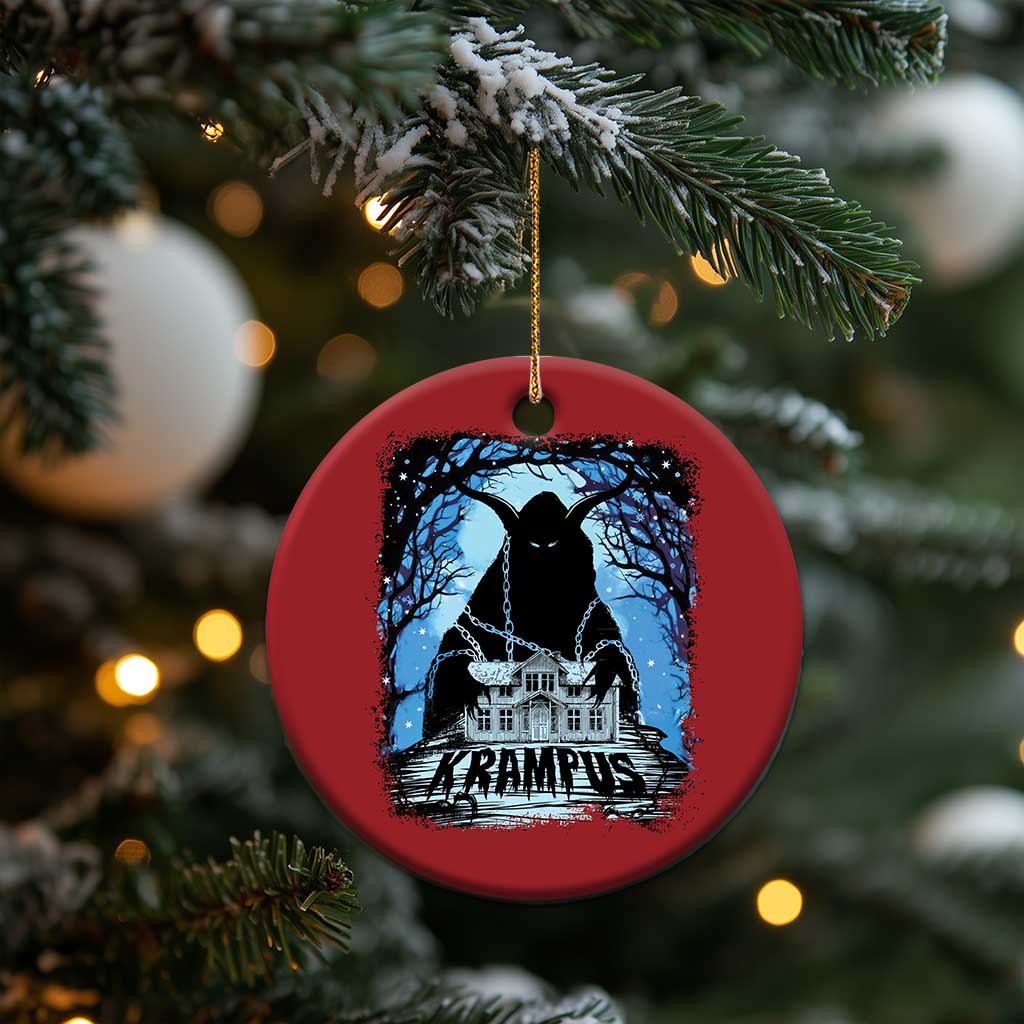 Red circular Krampus ornament with blue haunted house graphic hanging from pine branches