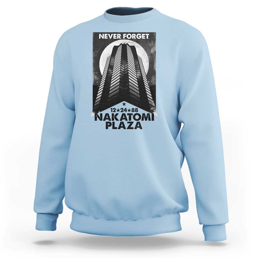 Light blue crewneck sweatshirt with front graphic print reading “NEVER FORGET” and “NAKATOMI PLAZA”