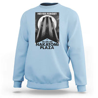 Light blue crewneck sweatshirt with front graphic print reading “NEVER FORGET” and “NAKATOMI PLAZA”