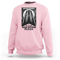 Light pink crewneck sweatshirt with front graphic print reading “NEVER FORGET” and “NAKATOMI PLAZA”