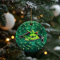 Green circular cat Christmas ornament with neon cartoon cat face, hanging on a tree branch.