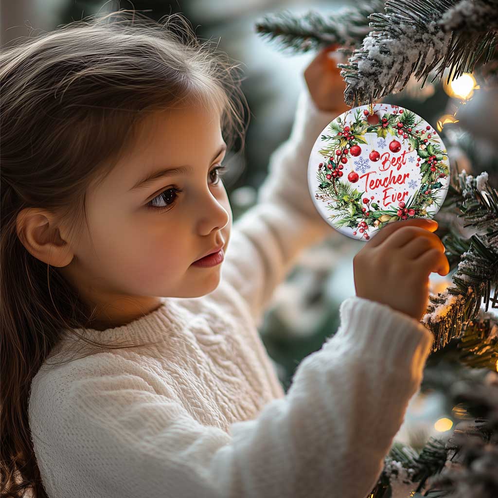 Round “Best Teacher Ever” Christmas ornament with holly and pine, hanging from a child’s hands