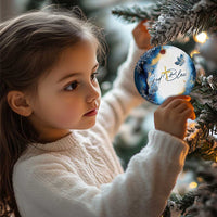 Blue and white round “God Bless” ornament with gold cross, hanging on a tree