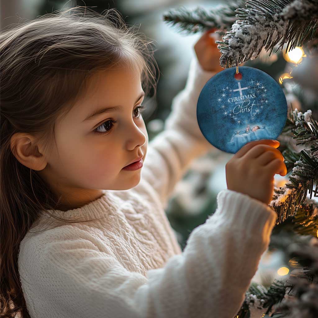 Child holding a blue round ornament with cross and 'Christmas begins with Christ' text