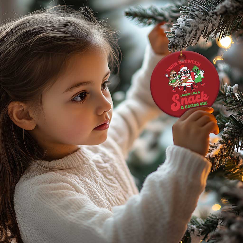 Red round Christmas ornament hanging on tree branch with cartoon “Torn Between” snack design