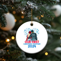 White round Christmas ornament hanging on a tree branch with couple graphic and “Our First Christmas Together 2024”