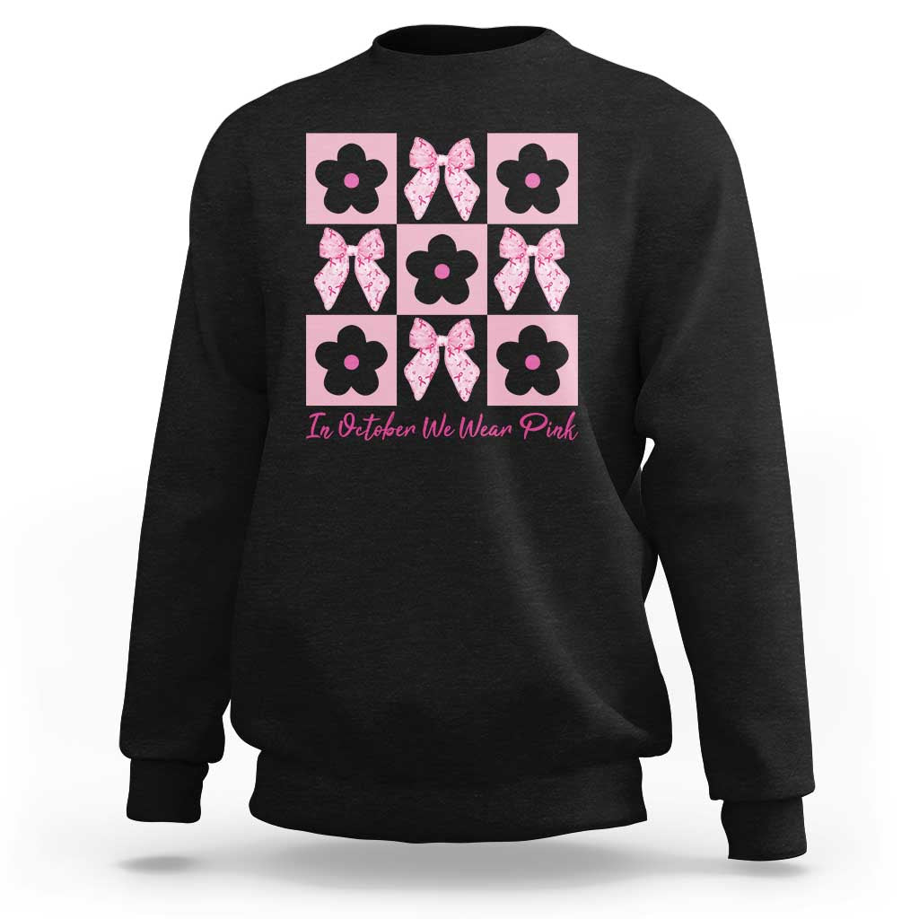 Black crewneck sweatshirt with pink floral bow grid and “In October We Wear Pink” text