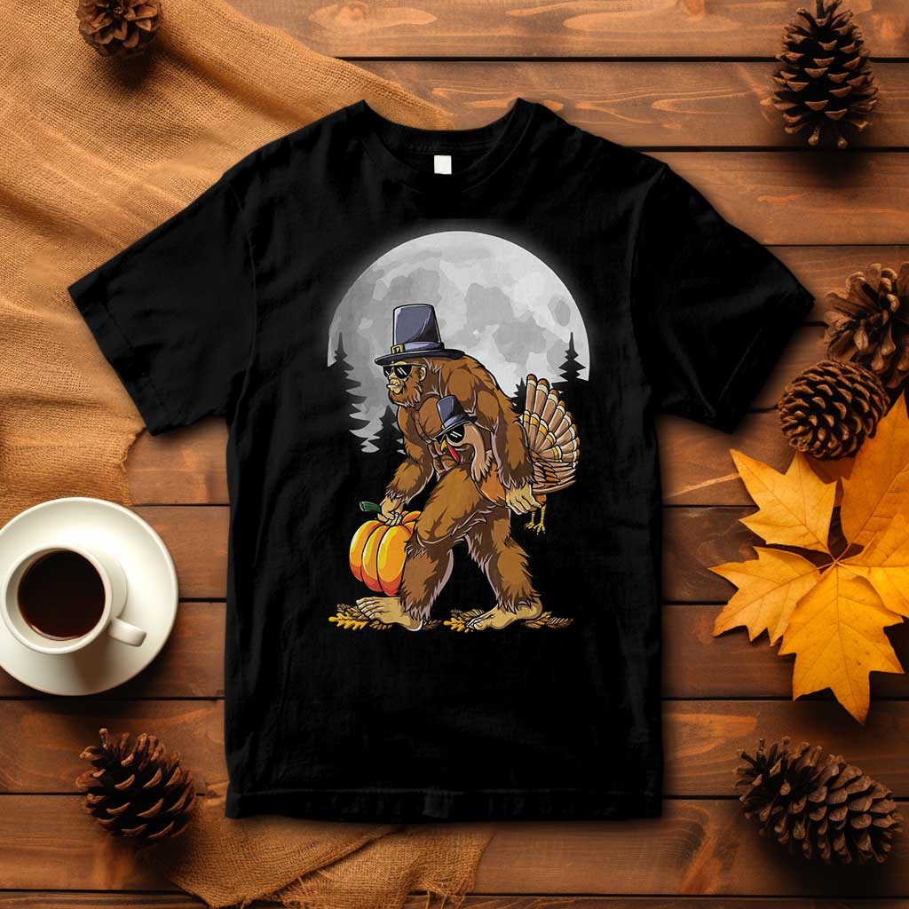 Black T-shirt with pilgrim sasquatch holding turkey and pumpkin graphic