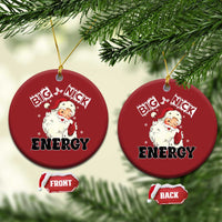 Two red round Santa “Big Nick Energy” ornaments hanging from tree branches