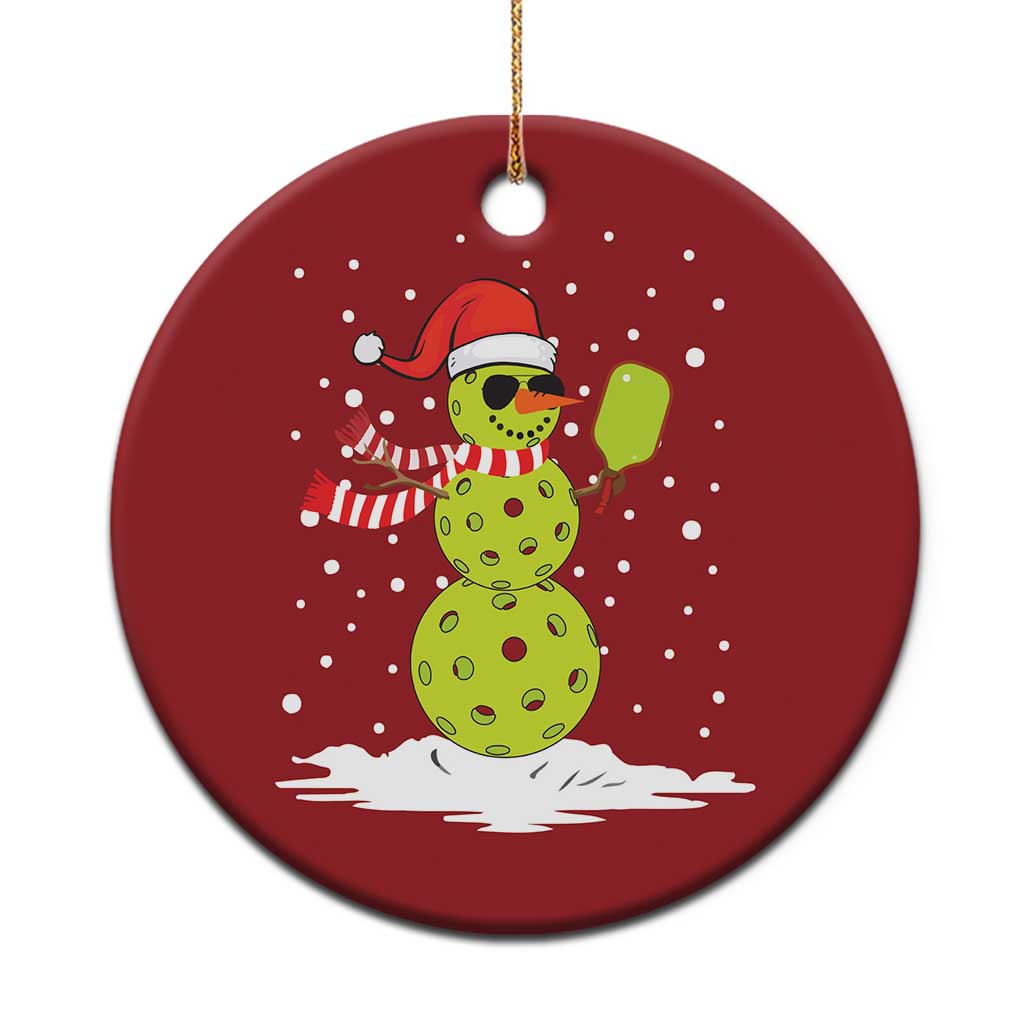 Red round Christmas ornament with a cartoon snowman holding a paddle, gold hanging loop