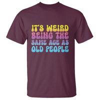 Maroon T-shirt with colorful slogan graphic: weird being same age as old people