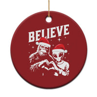 Red round Christmas ornament with “BELIEVE” and an alien and Bigfoot graphic