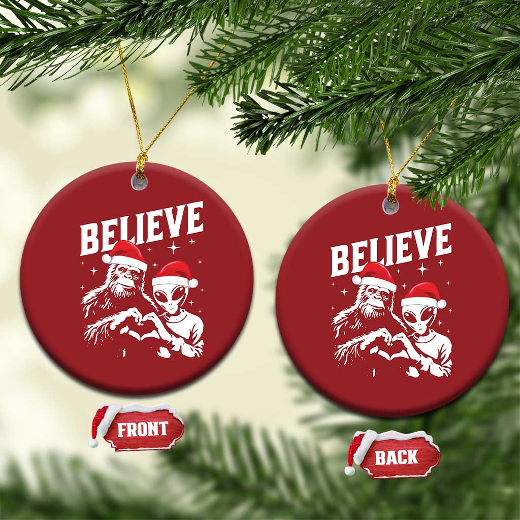 Two red round “BELIEVE” ornaments with alien and Bigfoot designs, hanging from tree