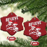 Two red heart-shaped Christmas ornaments with “BELIEVE” and alien and Bigfoot designs