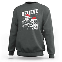 Dark heather crewneck sweatshirt with 'Believe' alien and Bigfoot holiday graphic