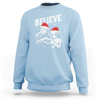 Light blue crewneck sweatshirt with 'Believe' alien and Bigfoot holiday graphic