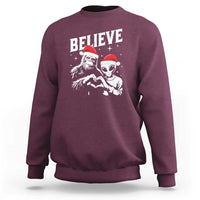 Maroon crewneck sweatshirt with 'Believe' alien and Bigfoot holiday graphic