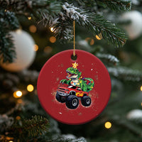 Red circular Christmas ornament featuring a green dinosaur and monster truck, on a tree branch.