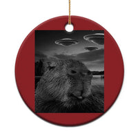 Red round Christmas ornament with capybara selfie and UFOs, hanging on gold loop.