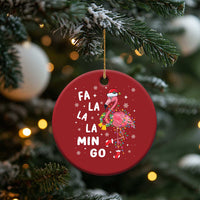 Red round flamingo Christmas ornament hanging from a pine tree branch with “FA LA LA MIN GO”.