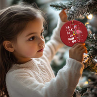 Red round flamingo Christmas ornament held by a child, featuring “FA LA LA MIN GO”.