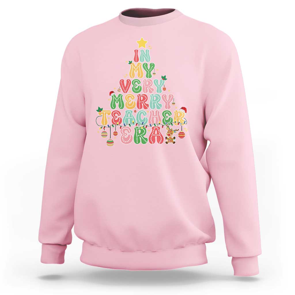 Light pink teacher sweatshirt with colorful “Merry Teacher” holiday graphic on front.