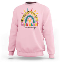 Light pink back-to-school sweatshirt with rainbow leopard graphic and “WILD ABOUT learning” text