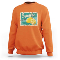Orange crewneck sweatshirt with front “Squeeze the Day” lemon graphic