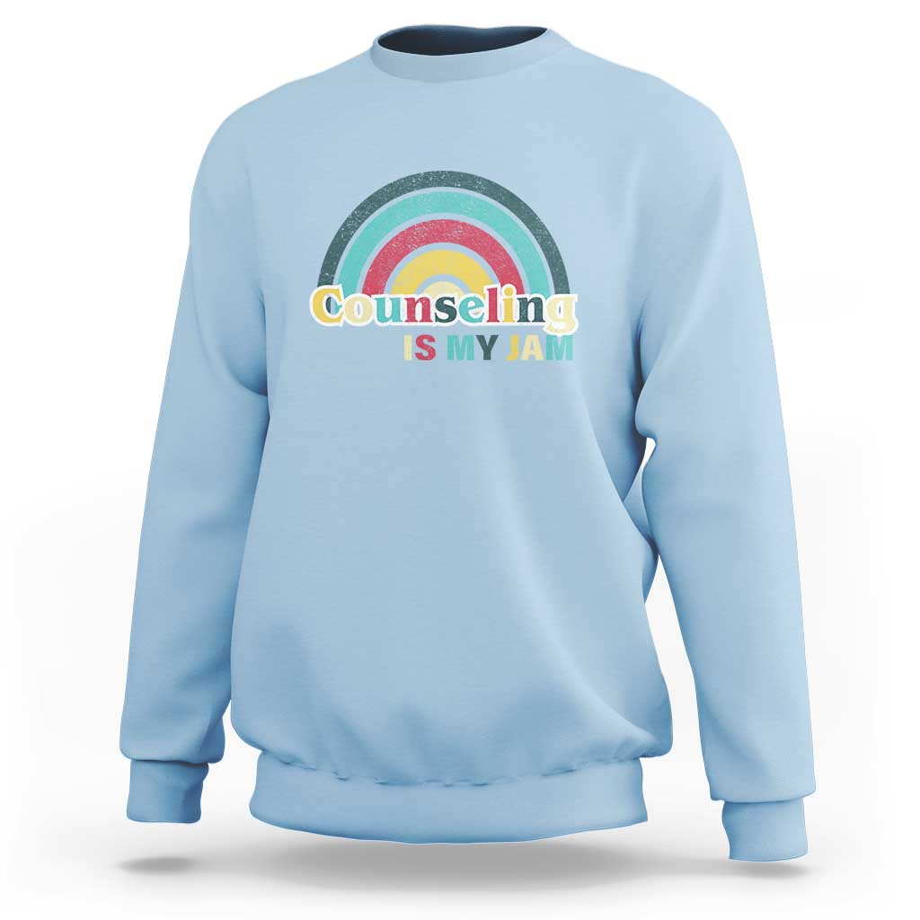 Light blue sweatshirt with ribbed crew neck and front rainbow “Counseling Is My Jam” graphic