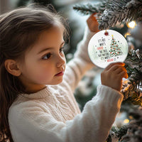 White circular Christmas ornament with tree quote, held by a child on a Christmas tree