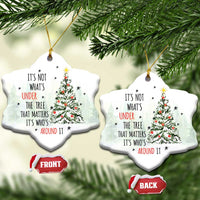 Two white heart-shaped Christmas ornaments with tree and quote, hanging on evergreen branches