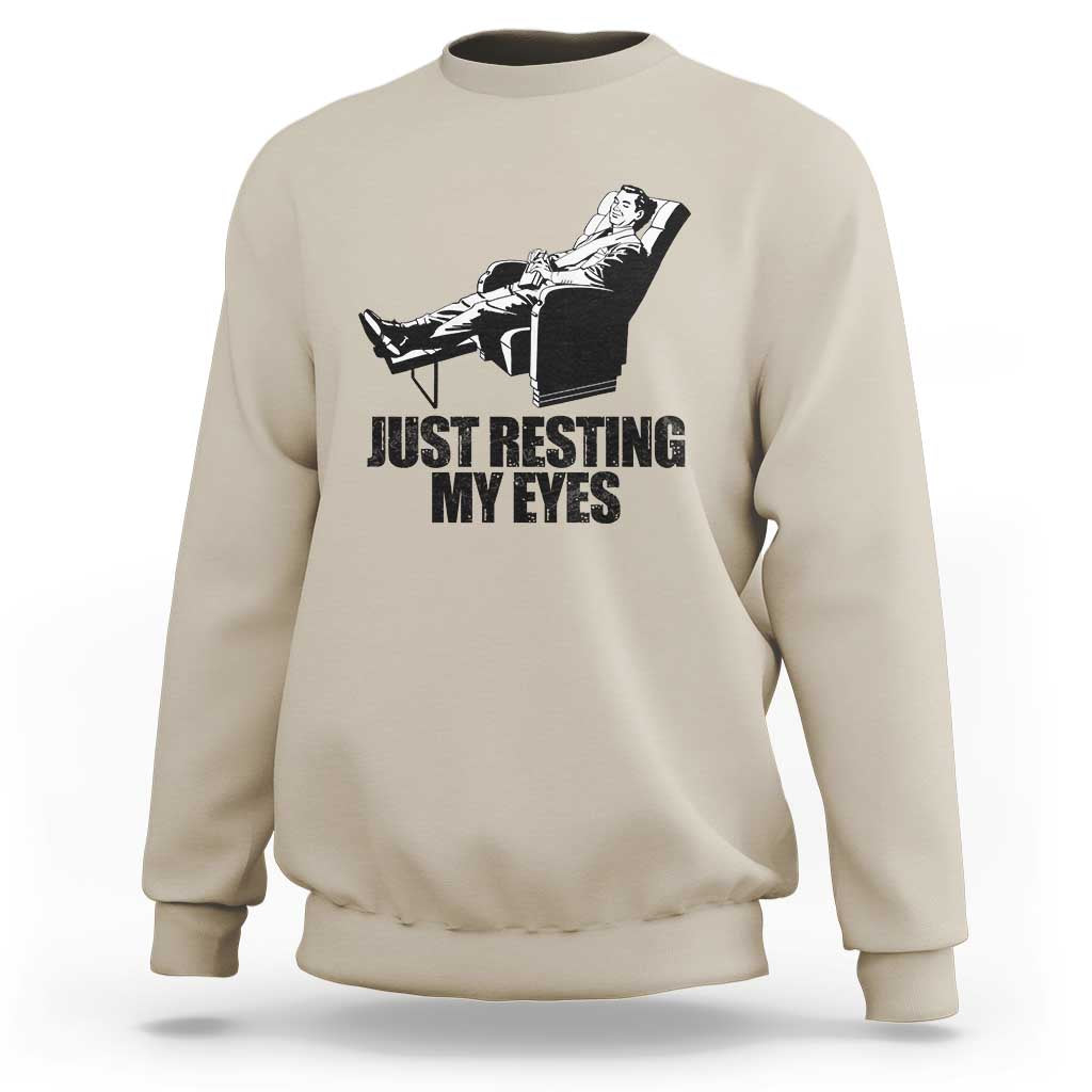Beige crewneck sweatshirt with “JUST RESTING MY EYES” graphic and cat on a chair