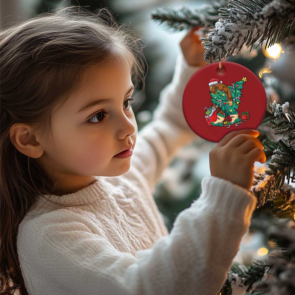 Red round ornament on a Christmas tree with cartoon Bigfoot Santa scene.