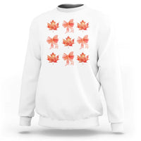 White crewneck sweatshirt with orange bow and maple leaf graphic print.