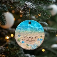 Personalized engagement Christmas ornament, round beach ocean design with “Engaged” and “JAMES & EMILY”.