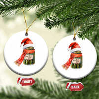 Round Christmas ornament showing pickle jar in Santa hat and scarf; front and back text